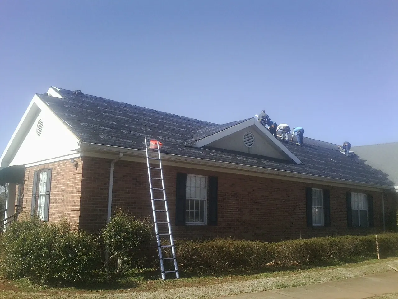 Crew tearing shingles off a brick ranch roof with a ladder set — Emergency Roof Repair work by our crew in Emmett