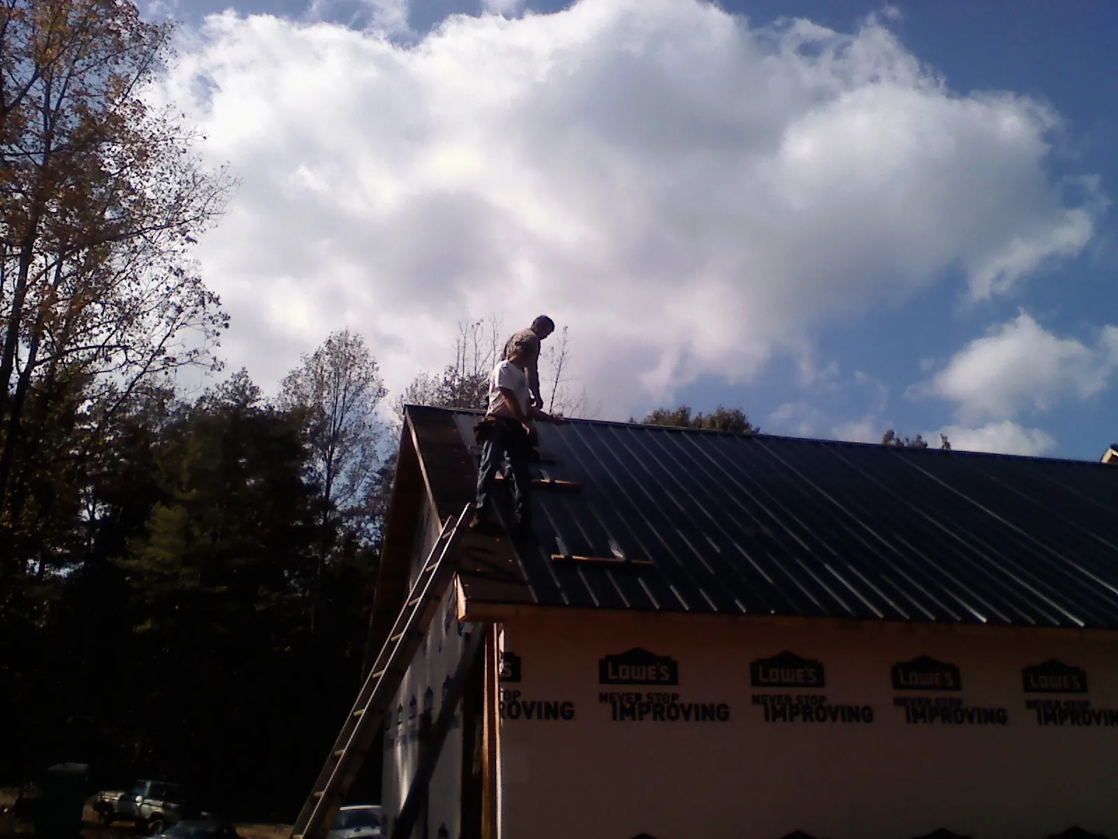 Roofer fastening dark metal panels high against a cloudy sky, from a Roof Inspection job in Emmett