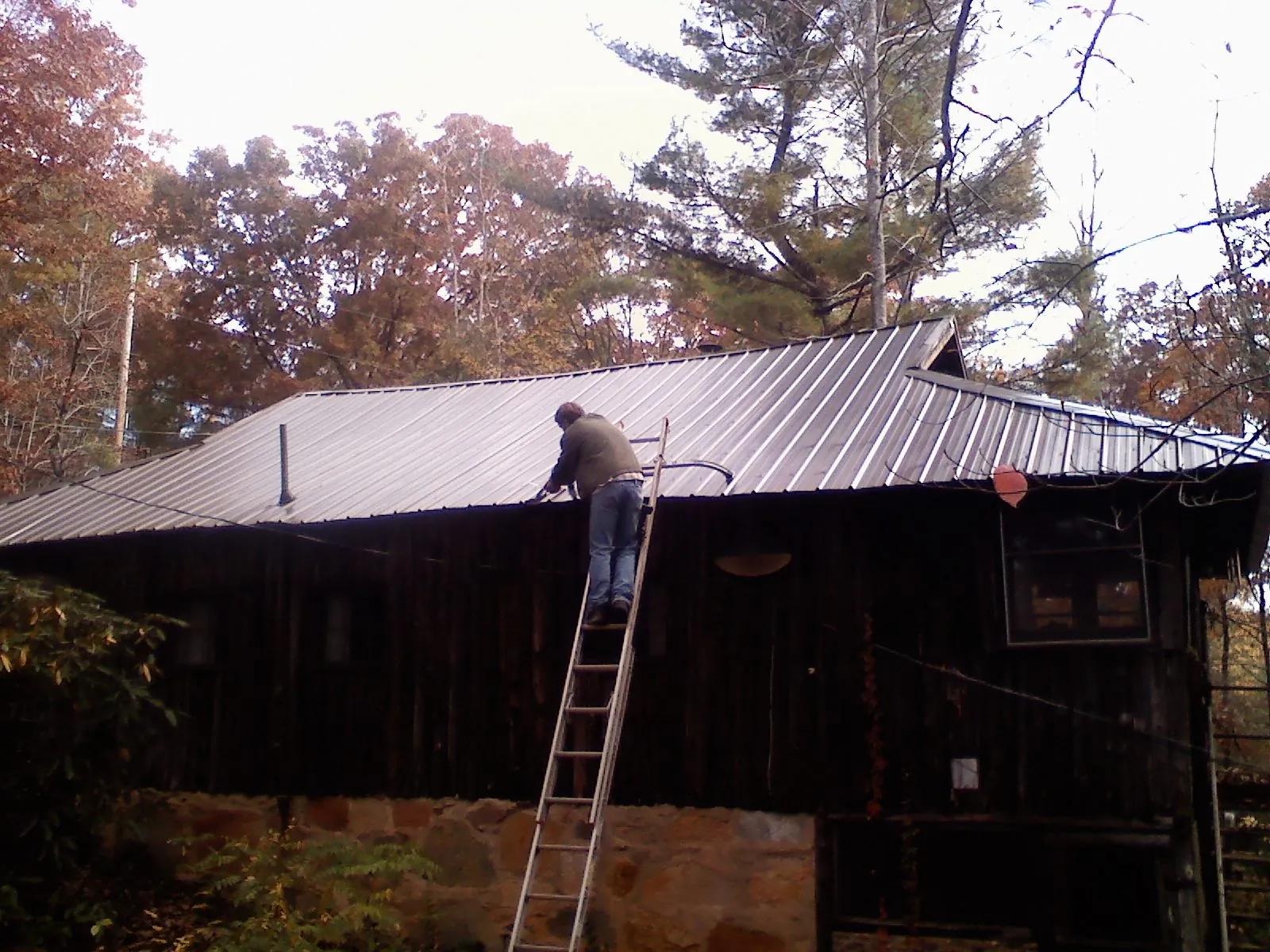 Roofer on a ladder working along the edge of a cabin metal roof in Emmett